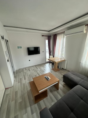 A modern living room with a flat-screen TV, a wooden coffee table, a sofa, and a dining table.