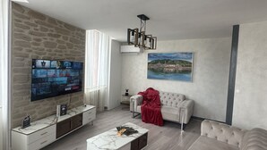 Ein modernes Wohnzimmer mit einer Wand aus Stein, einem Flachbildfernseher, einem weißen Sofa, einer roten Decke und einem Landschaftsbild.