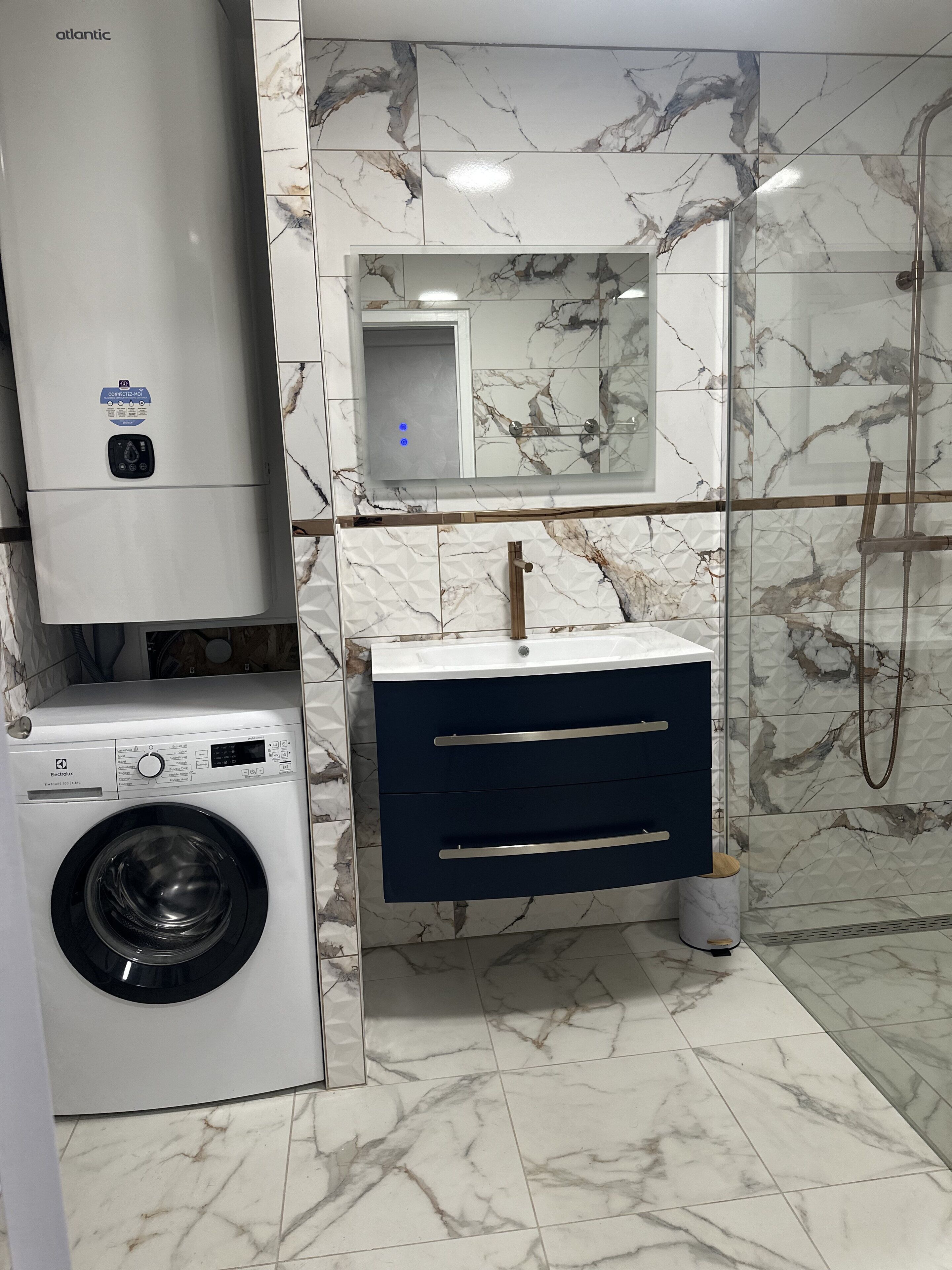 Une petite salle de bain équipée d’un lave-linge, d’un meuble-lavabo avec des tiroirs et d’un espace douche.