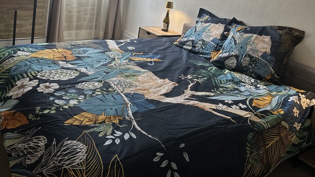 Ein Schlafzimmer mit einem Bett, einem Nachttisch, einer Lampe und einem Fenster mit Vorhängen.