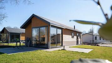 A modern two-story house with a large glass door entrance, a patio with outdoor furniture, and a well-maintained lawn.