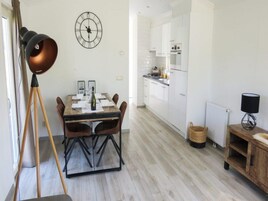Una cocina moderna con armarios blancos, una mesa de comedor para cuatro personas y un reloj en la pared.
