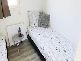 Una habitación pequeña con cama individual, un radiador, una mesa con lámpara y una ventana con cortinas.