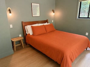 Quarto com cama de madeira, uma pequena mesa de cabeceira e duas luzes fixadas na parede.