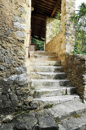 Un escalier en pierre menant à une porte en bois, entouré de murs de pierre et de végétation.