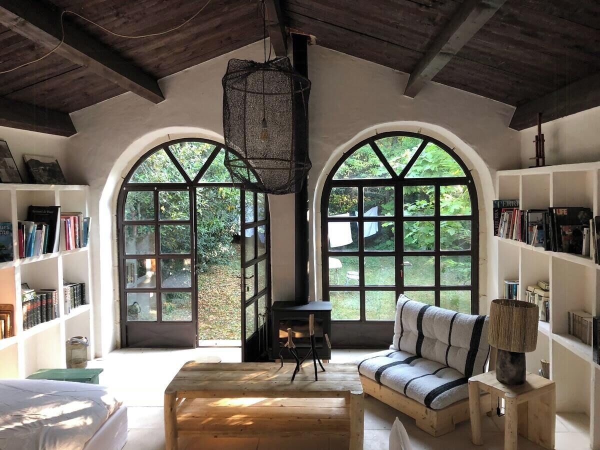 A cozy reading nook with a sofa, a small table, and bookshelves, featuring large arched windows and a wooden ceiling.