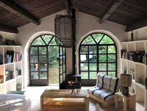A cozy reading nook with a sofa, a small table, and bookshelves, featuring large arched windows and a wooden ceiling. - 17th-century house below Saint-Montan castle (Saint-Montan)