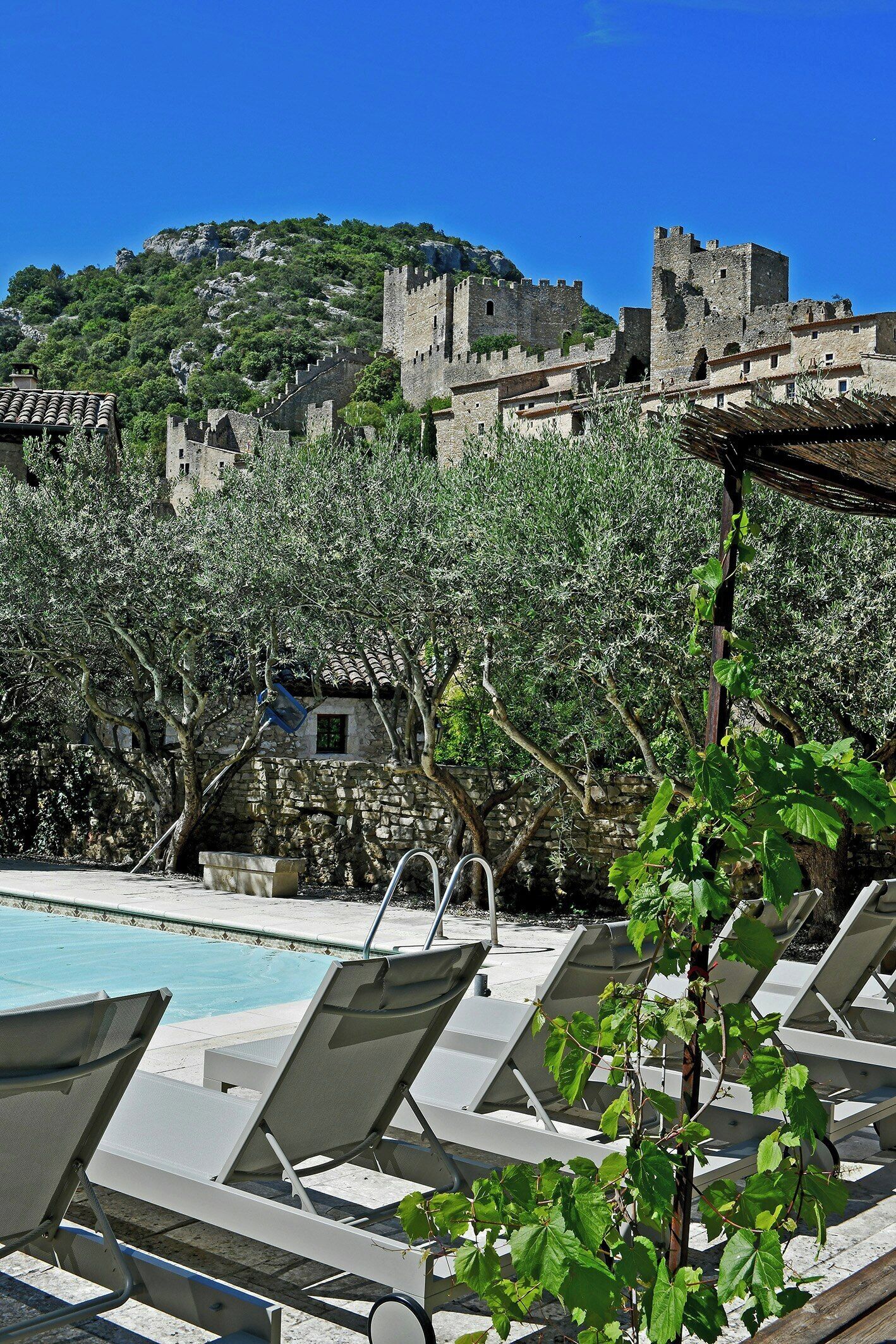 Un espace piscine avec des chaises longues, un mur en pierre et un château en arrière-plan.