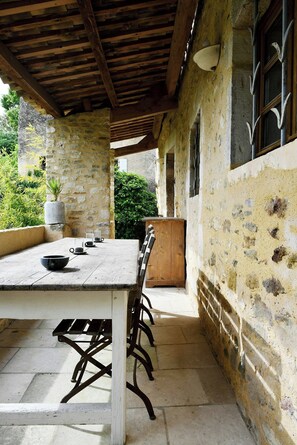 Une terrasse extérieure avec une table et des chaises, des murs en pierre et un plafond en bois.