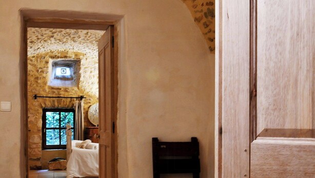 A corridor with a stone wall, a wooden door, and a bed with a white cover. - 17th-century house below Saint-Montan castle (Saint-Montan)