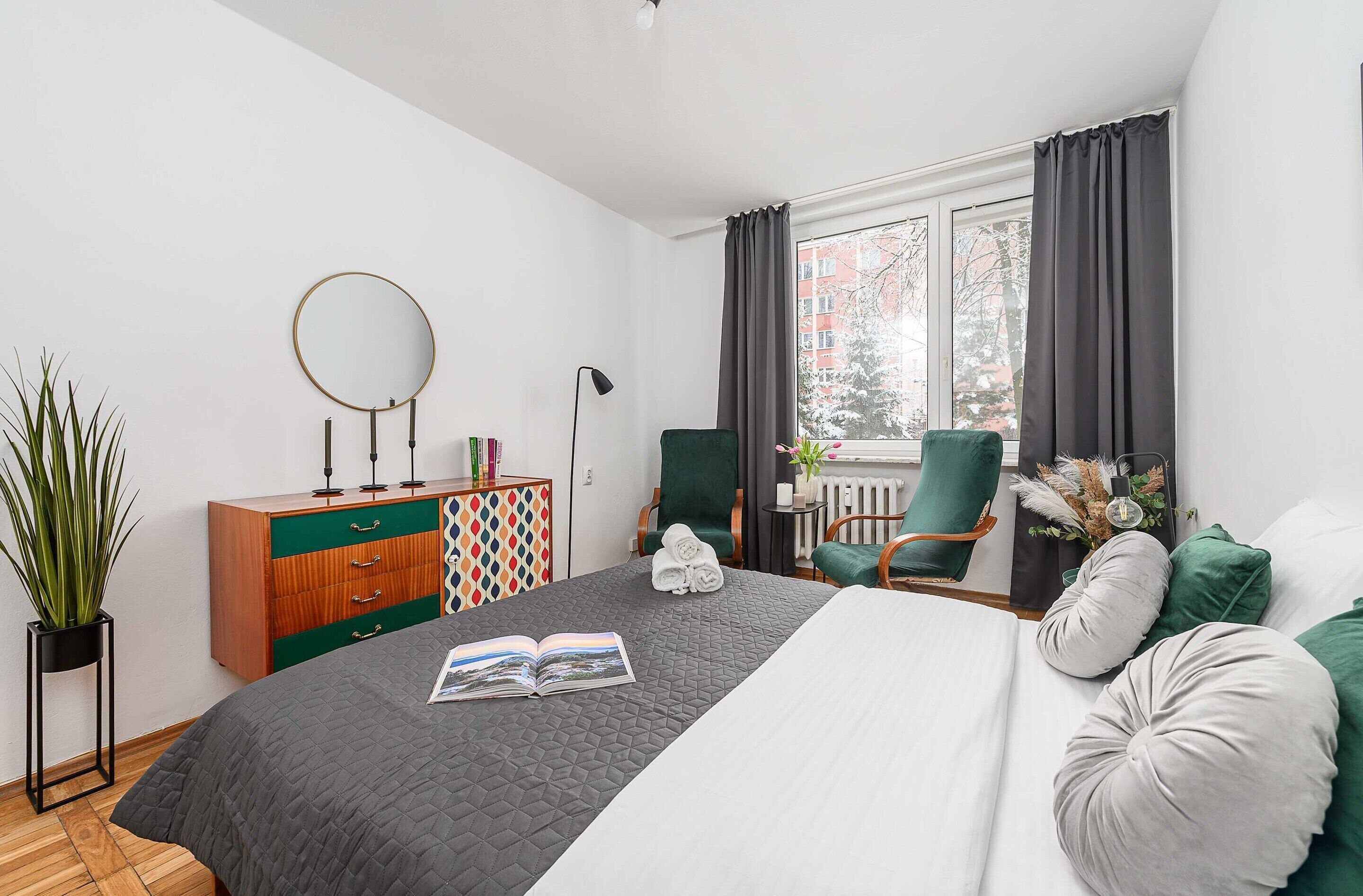 Ein modernes Schlafzimmer mit Bett, Kommode, Stuhl und einem Fenster mit Vorhängen.