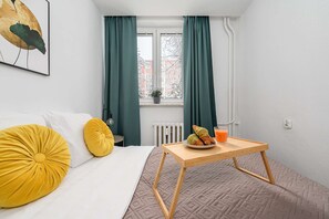 A bedroom with a bed, a bedside table with a plate of food and a glass of juice, and a window with curtains. - Family Stay on Boguckiego (Warsaw)