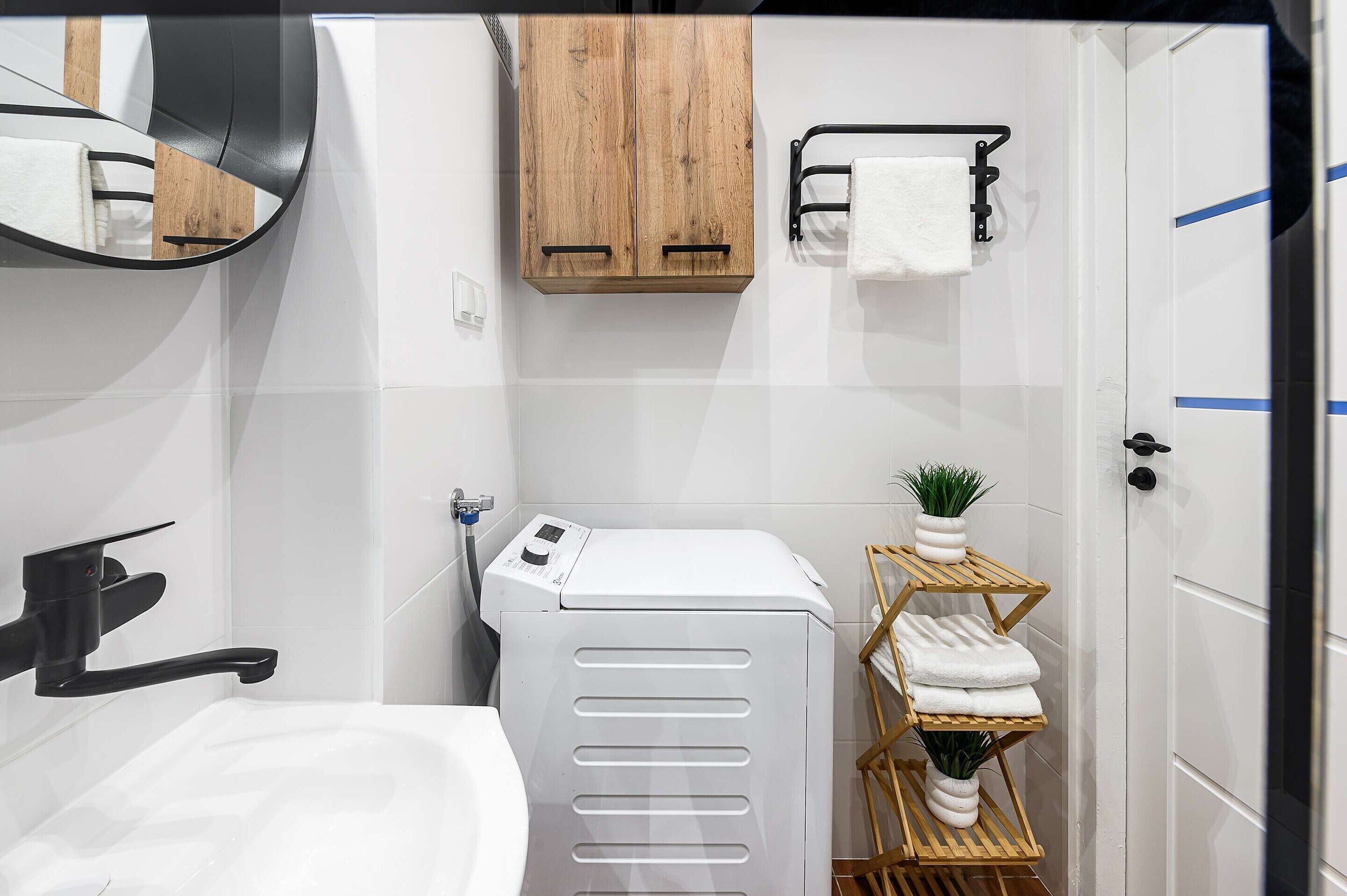 Une petite salle de bain équipée d’un lave-linge et d’un sèche-linge intégrés, d’un meuble en bois, d’un porte-serviettes et d’une petite plante posée sur une étagère.