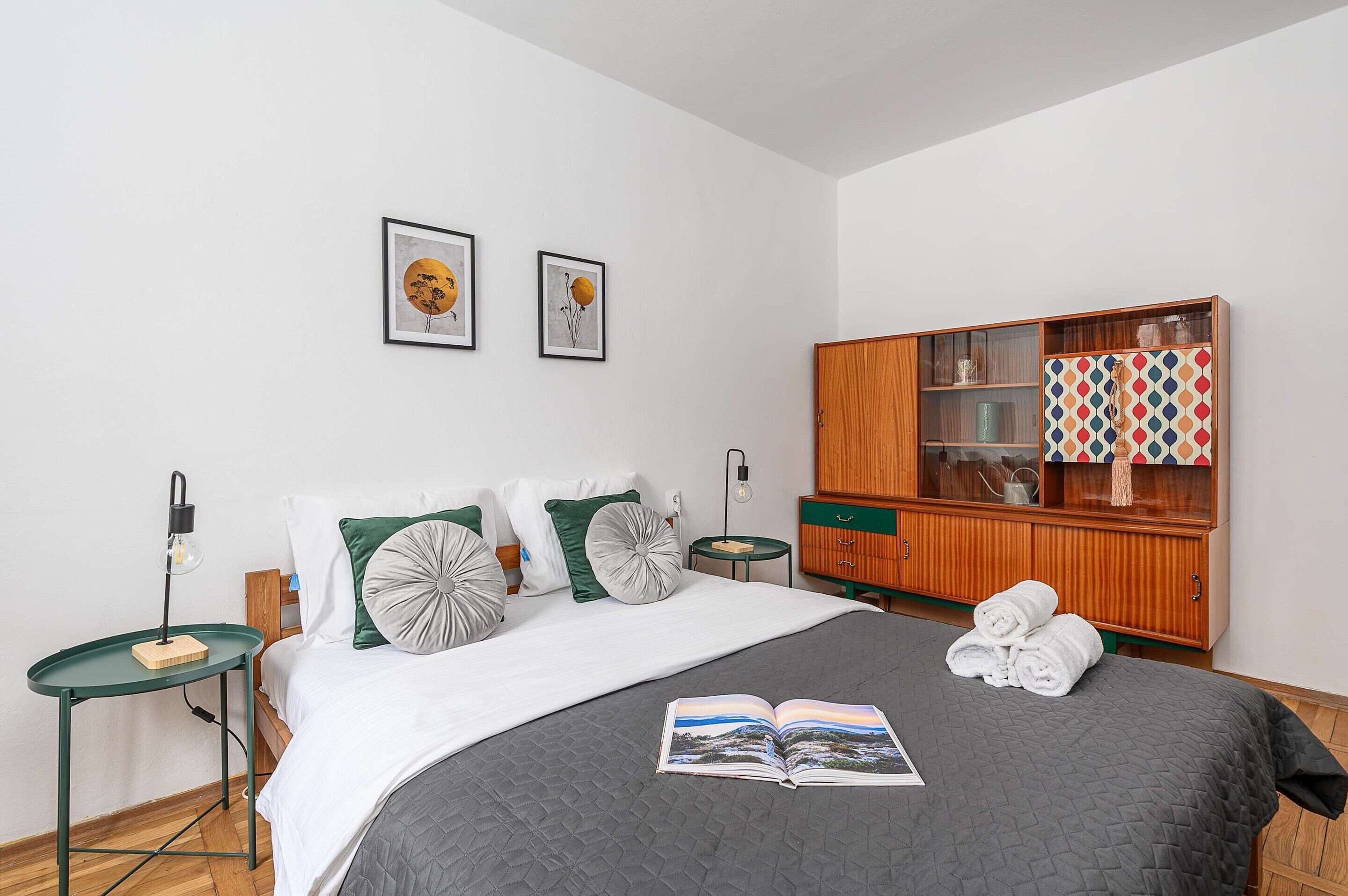 Une chambre à coucher bien rangée, avec un lit, des tables de chevet, une armoire en bois et deux œuvres d’art encadrées accrochées au mur.
