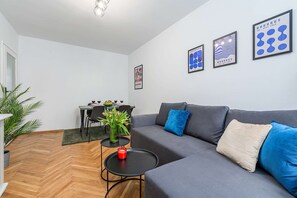 A modern living room with a grey sofa, a small round table with a red candle, and a dining area in the background. - Family Stay on Boguckiego (Warsaw)