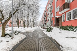 A snow-covered pathway flanked by trees and a red building with balconies. - Family Stay on Boguckiego (Warsaw)