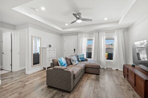Ein modernes Wohnzimmer mit einem Ecksofa, einem Deckenventilator und Blick ins Freie.
