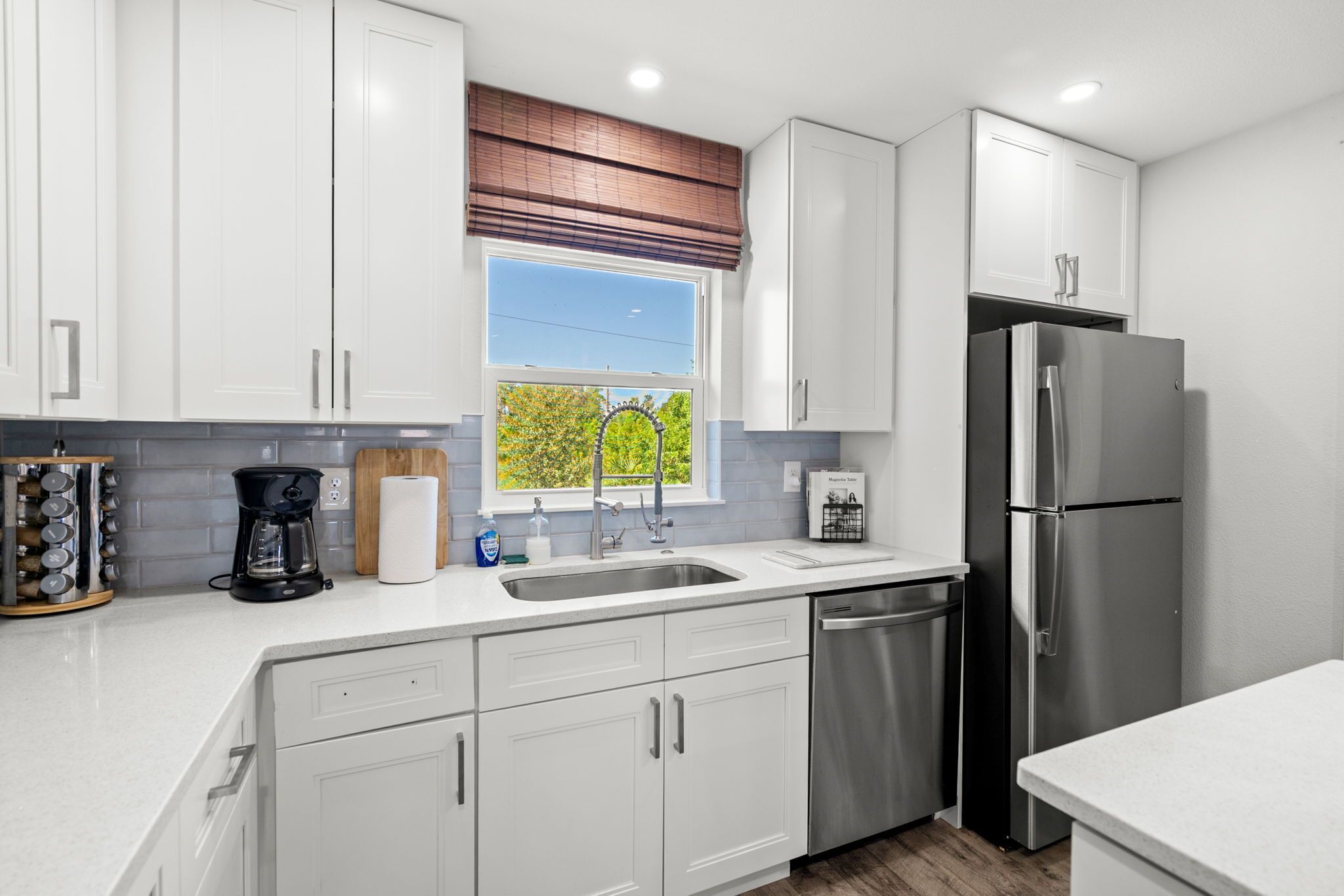 A modern kitchen with white cabinets, a stainless steel refrigerator, and a window with a view of greenery.