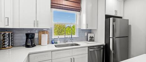 A modern kitchen with white cabinets, a stainless steel refrigerator, and a window with a view of greenery.