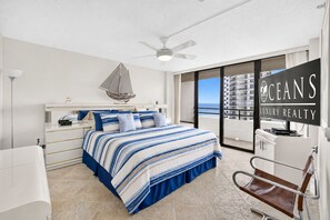 Ein Schlafzimmer mit Bett, Nachttisch, Schreibtisch, Stuhl, Deckenventilator und Meerblick.