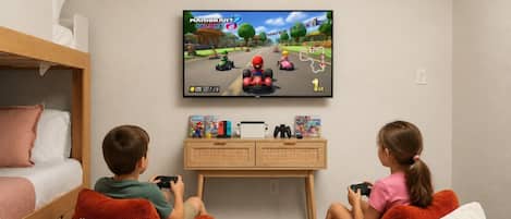 A room with a bed, a TV displaying a Mario Kart game, and two children playing.