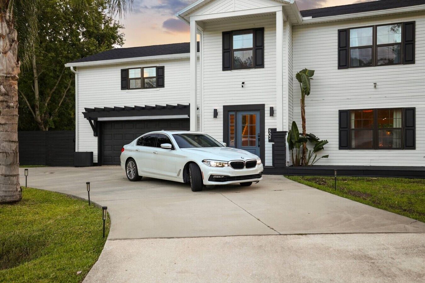 A white two-story house with a car parked in the driveway.