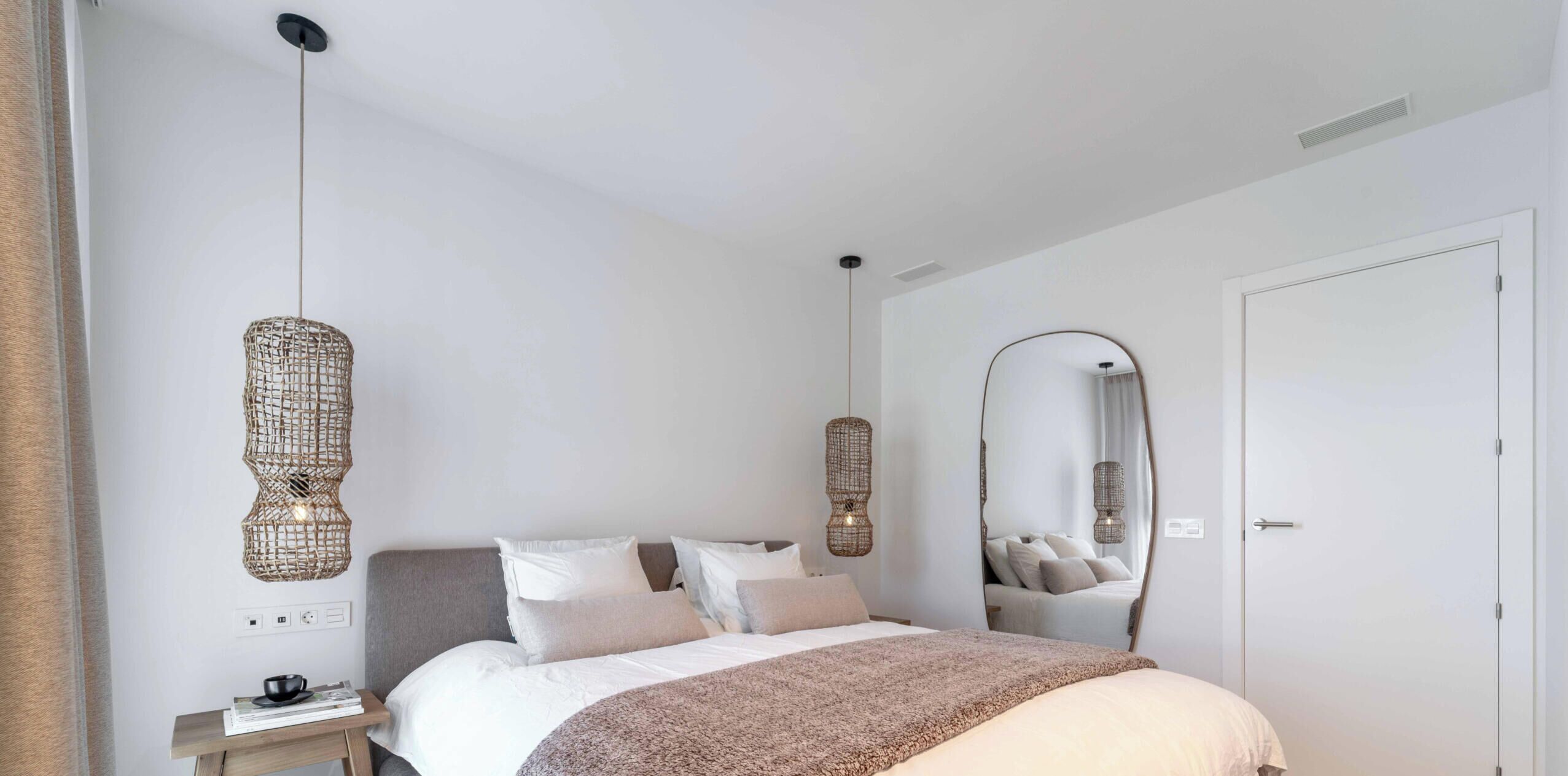 A minimalist bedroom with a bed, bedside table, and two hanging light fixtures.
