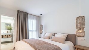 A bedroom with a bed, a bedside table, a hanging light fixture, and a view of a bathroom. - Infinity Blue – Rooftop Pool & Sea Views | Fuengirola (Fuengirola)