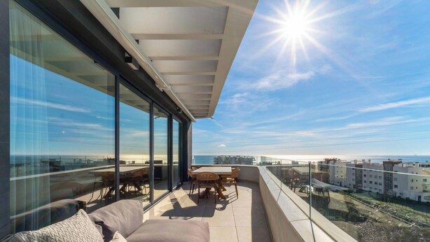 A balcony with a sofa and table, large windows, and a view of the city and sea. - Infinity Blue – Rooftop Pool & Sea Views | Fuengirola (Fuengirola)