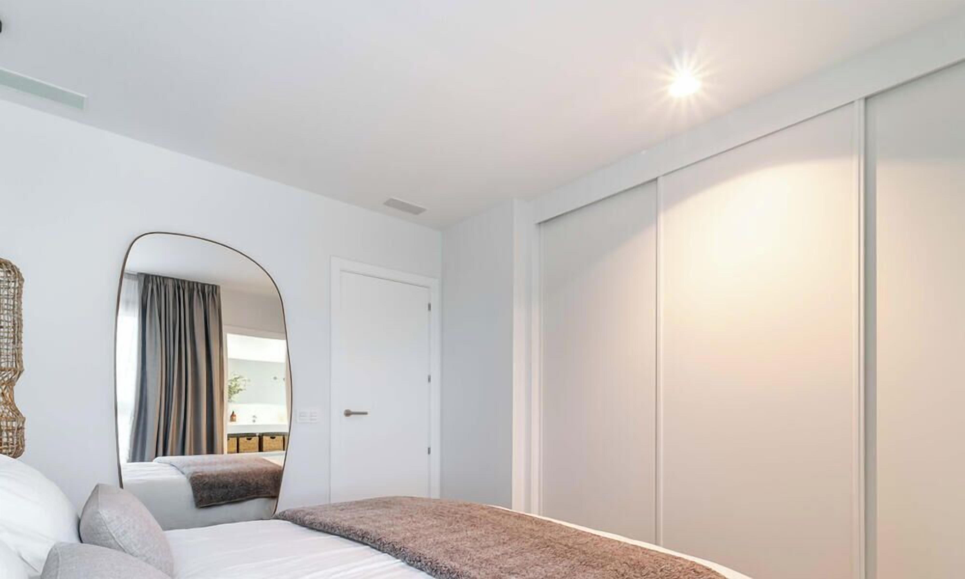 Une chambre à coucher comprenant un lit, une armoire, un miroir et donnant sur un balcon.
