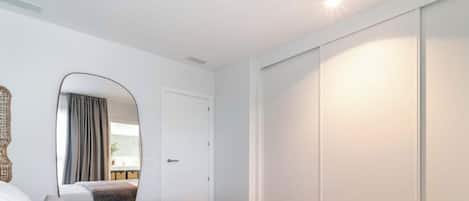 A bedroom with a bed, a wardrobe, a mirror, and a view of a balcony.