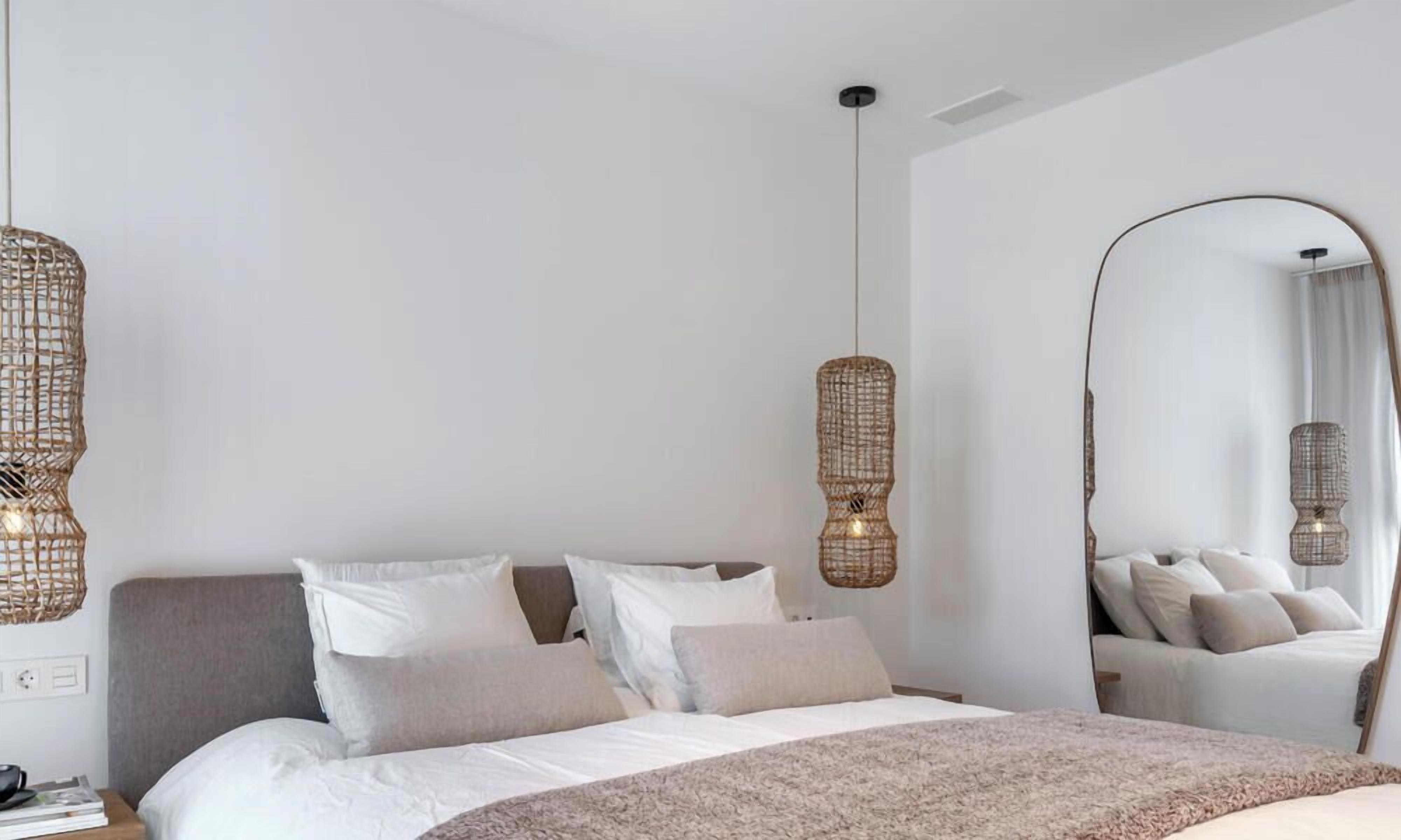 A modern bedroom with a large bed, two hanging wicker lamps, and a full-length mirror.