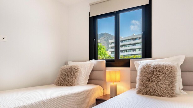 A hotel room with two beds, a window with a view of buildings, and a bedside lamp. - The Garden Escape 2bedroom garden unit (Fuengirola)