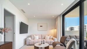 A modern living room with a sofa, a coffee table, and a TV mounted on the wall. - The Garden Escape 2bedroom garden unit (Fuengirola)