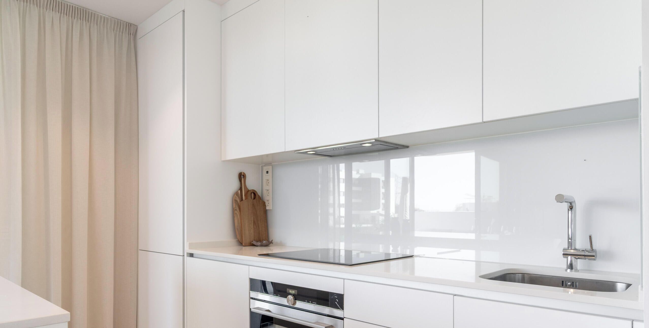 Een moderne keuken met witte kasten, een roestvrijstalen spoelbak en een ingebouwde oven.