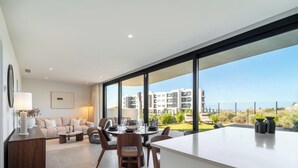 A modern living room with a dining area, large windows, and a view of buildings. - The Garden Escape 2bedroom garden unit (Fuengirola)