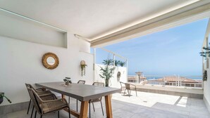 A balcony with a dining table and chairs, a hanging plant, and a view of the sea. - Casa Lara — Andalusian Village Retreat (Benalmádena)