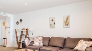 A modern living room with a brown sofa, decorative wall art, and a wooden shelf unit. - Casa Lara — Andalusian Village Retreat (Benalmádena)