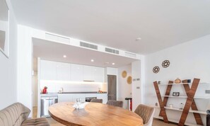A modern kitchen with white cabinets, a stainless steel refrigerator, and a wooden dining table with chairs. - Casa Lara — Andalusian Village Retreat (Benalmádena)