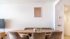 A modern dining area with a wooden table and cushioned chairs, a mounted flat-screen TV, and a plain wall with a single framed artwork. - Casa Lara — Andalusian Village Retreat (Benalmádena)