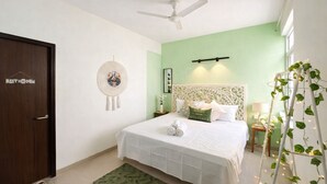 Quarto com cama, ventoinha no teto, mesa de cabeceira, luminária de apoio, arte pendurada na parede, um sonho apanhador e uma porta com a inscrição 'BATHROOM'.