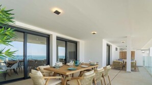 A modern dining area with a large table set for six, surrounded by wicker chairs, and a view of the sea through large glass doors. - Casa Lisa-New 3bed with stunning Sea-views in Fuengirola (Fuengirola)