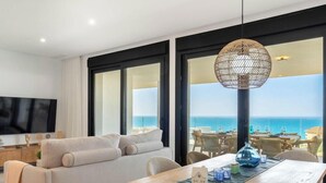 A modern living room with a large flat-screen TV, a sofa, and a dining area with a table set for two. - Casa Lisa-New 3bed with stunning Sea-views in Fuengirola (Fuengirola)