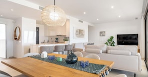 Ein modernes Wohnzimmer mit einem Holzesstisch, grauen Sofas und einem großen Fernseher.