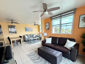 A living room with a sofa, a coffee table, a dining table with chairs, a ceiling fan, and artwork on the walls. - 3-bedroom condo in beach town of Rincón with pool and AC at Sea Beach Village (Rincón)