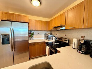 A kitchen with wooden cabinets, stainless steel appliances, a microwave, a stove, and a coffee maker. - 3-bedroom condo in beach town of Rincón with pool and AC at Sea Beach Village (Rincón)