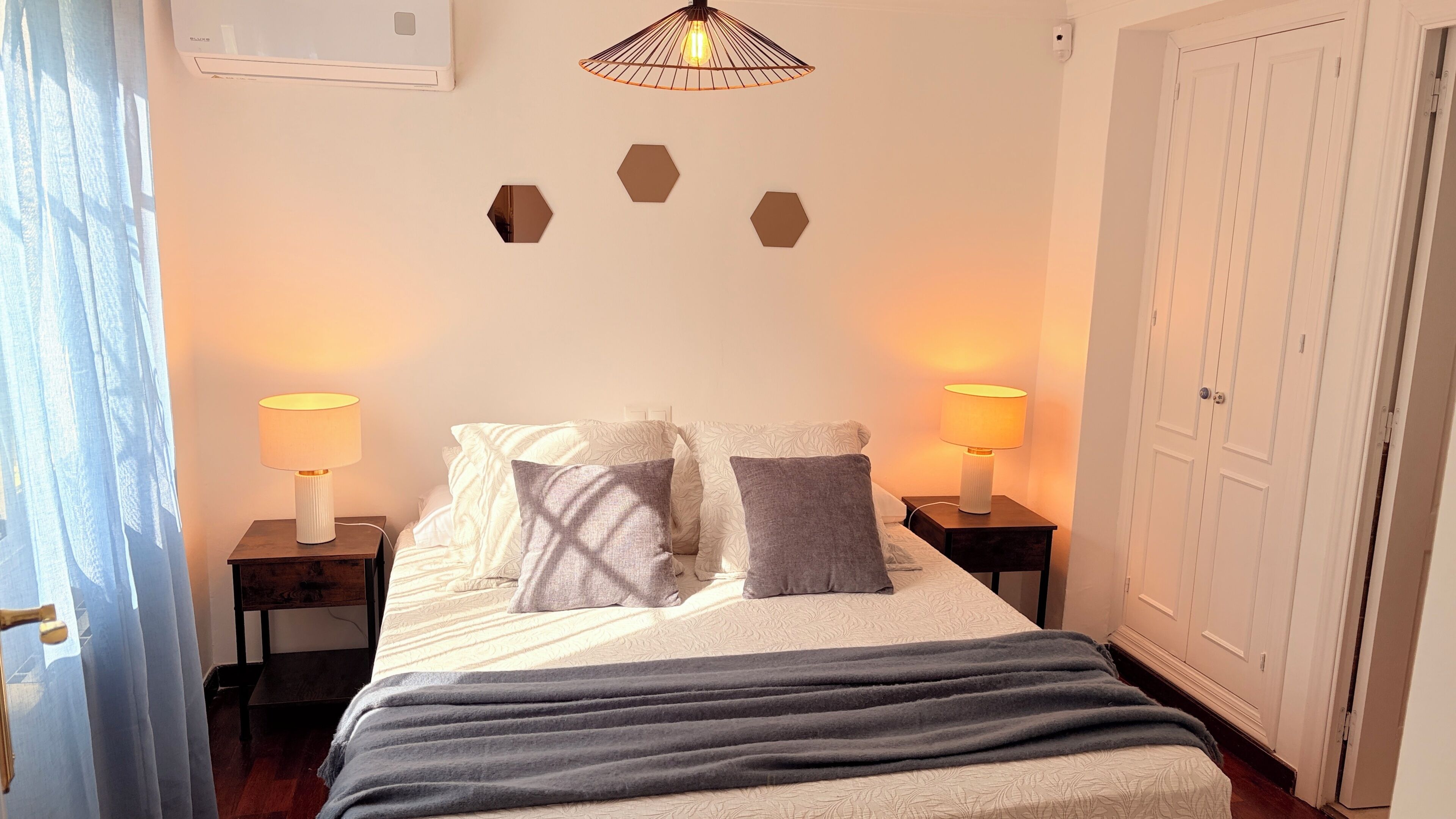 A bedroom with a bed, two bedside lamps, a ceiling light fixture, and a wardrobe.