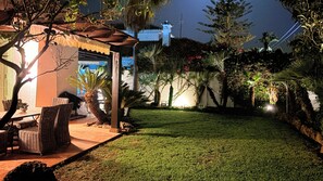 A well-lit outdoor area with a grassy lawn, seating area with wicker furniture, and a variety of plants and trees. - Lovely 3-bedroom house in Marbella perfect for relaxing getaways (Marbella)