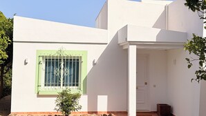 Una casa moderna de dos pisos con fachada blanca, un ventanal verde y un pequeño jardín con un sendero que lleva a la entrada.