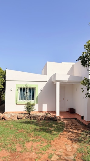 Ein modernes, zweistöckiges Haus mit weißer Fassade, einem grünen Fenster und einem kleinen Gartenbereich mit einem Weg zum Eingang.